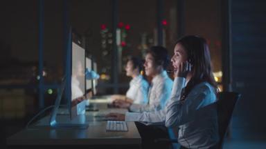 千年亚洲青年呼叫中心团队或客户服务主管在深夜办公室使用电脑和麦克风耳机提供工作技术支持。电话推销或销售工作概念.